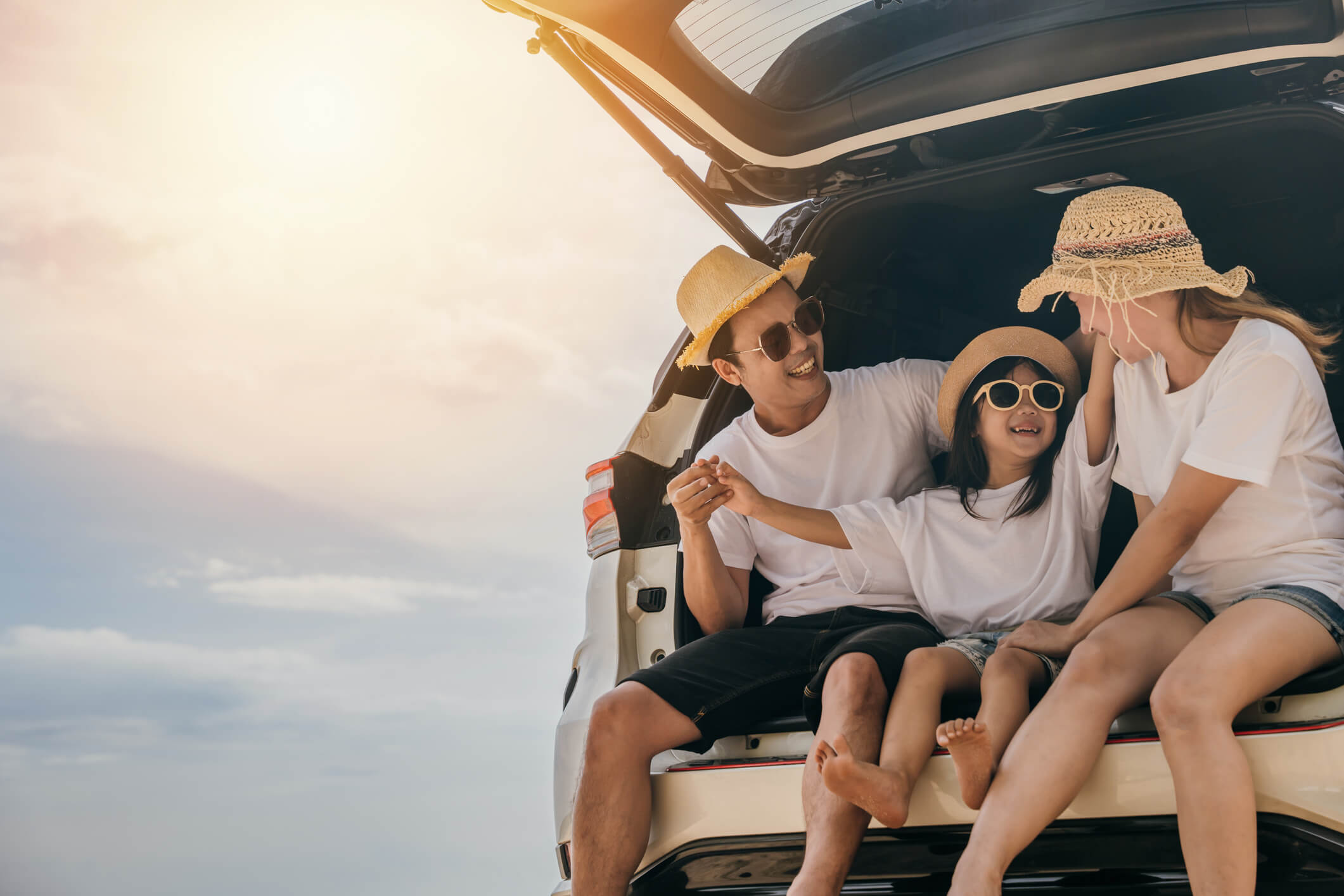 Smiling family in straw hats sitting in the open trunk