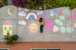 Boy at home, sheltering in place occupying time by drawing on sidewalk with chalk.
